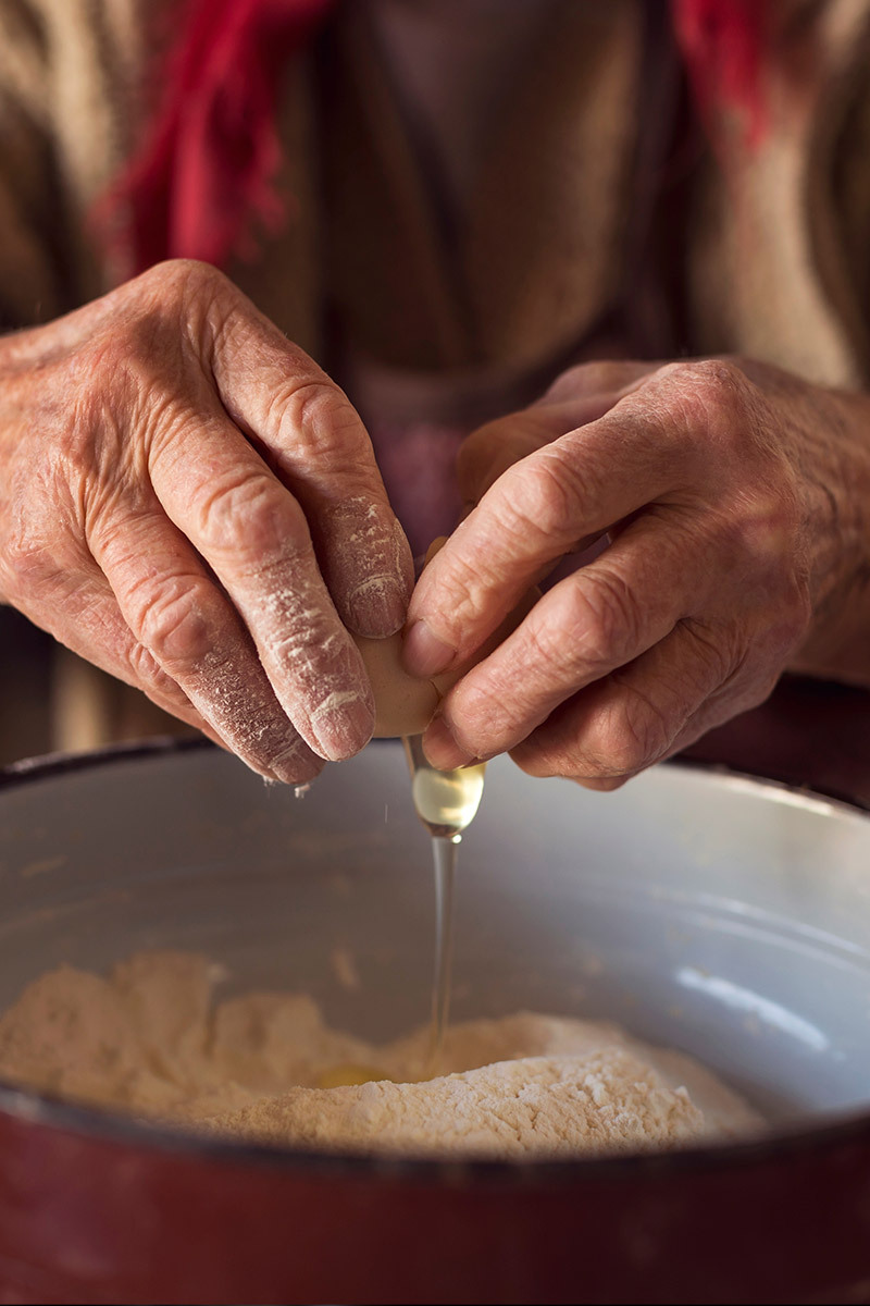 Elderly hands cracking an egg into a bowl of flour
