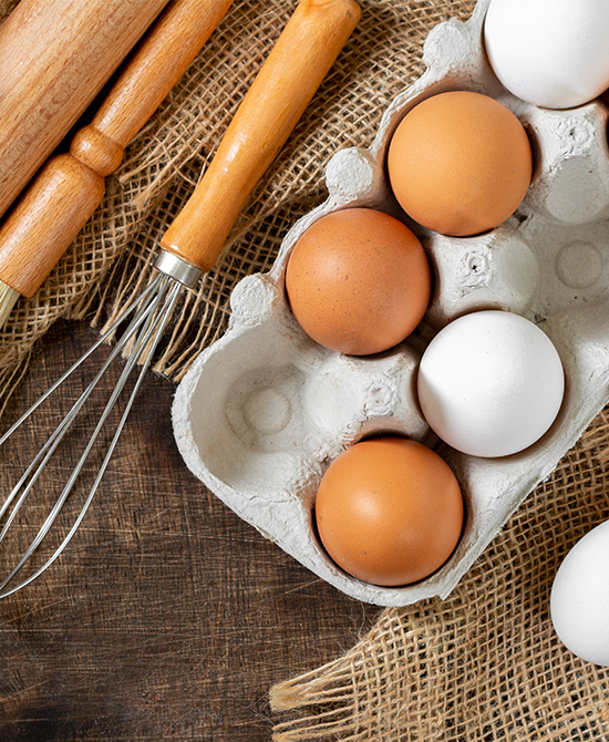 close up of brown and white eggs in a carton next to kitchen utensils