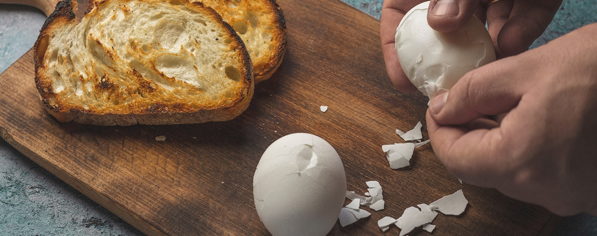 Hands peeling hard boiled white eggs on cutting board