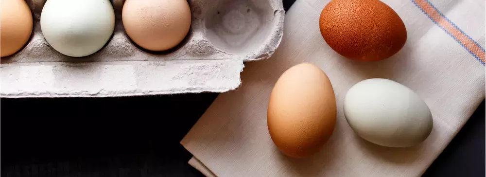 One white egg and two brown eggs sitting on white napkin