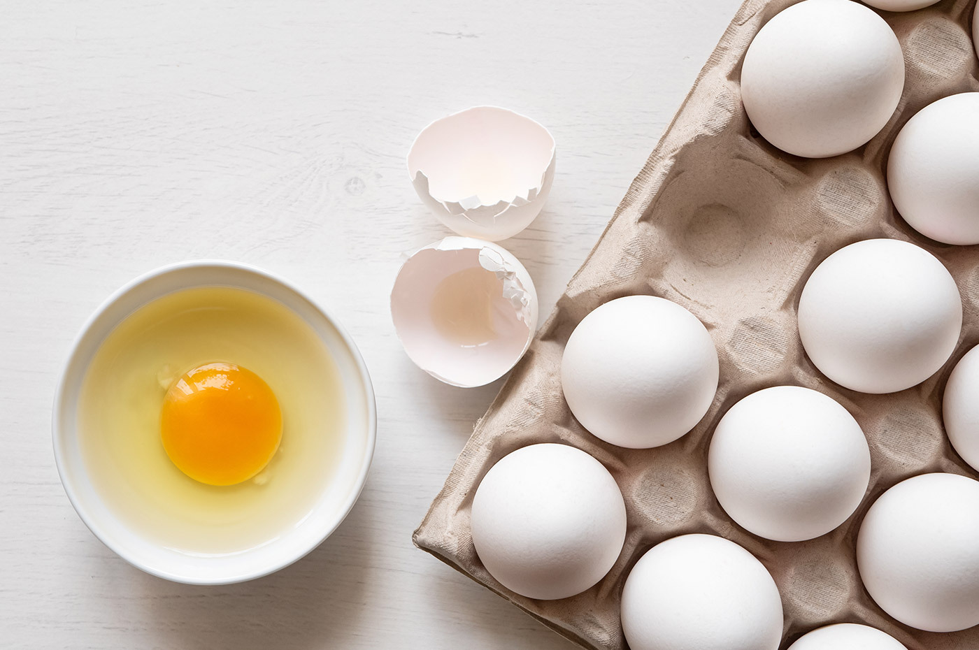 Cracked egg in a bowl next to full egg carton